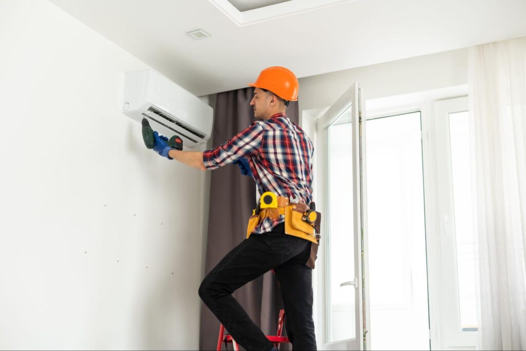 An AC installer installing a wall-mounted air conditioning system in a home.