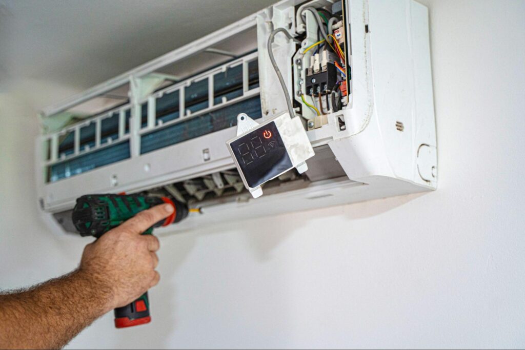 A close-up of an AC installer using a drill to install an air conditioner on the wall of a home.