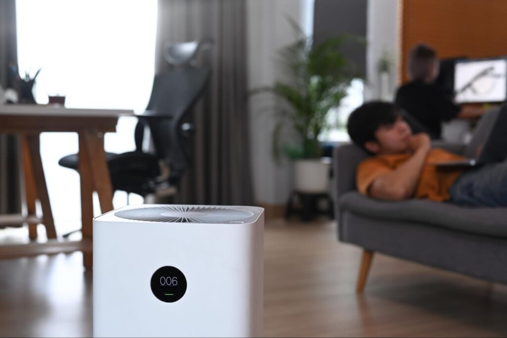 A man laying on the living room couch on his laptop with an air purification system beside him.